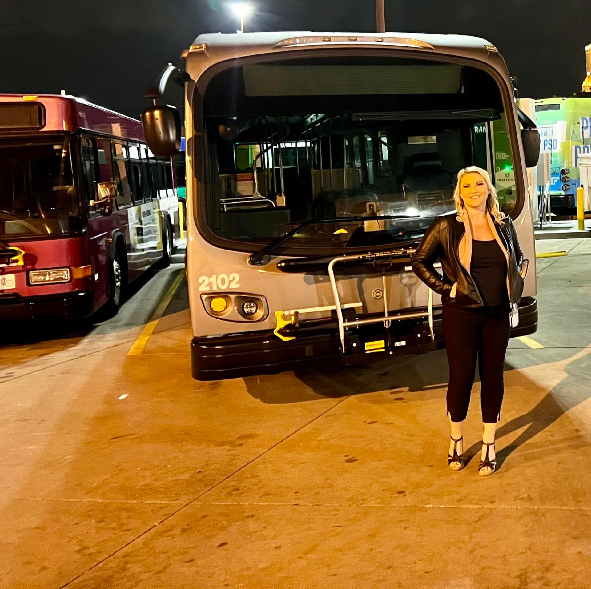 Michelle Robertson of Grand Splash Marketing standing beside a transit bus at an agency operations facility at night